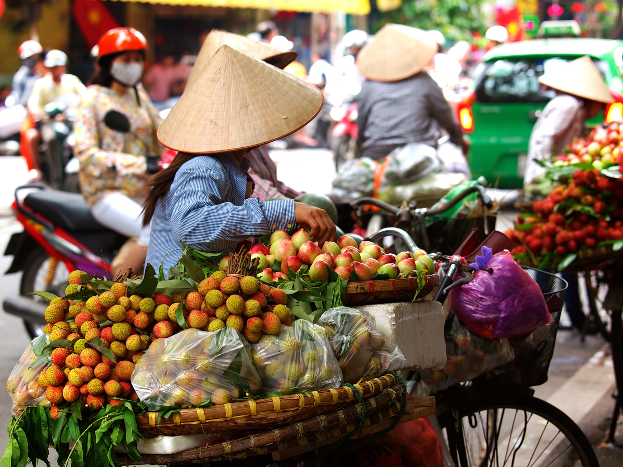 Straßenmarkt in Hanoi, Vietnam: Obsthändler mit Fahrrädern und traditionellen vietnamesischen Hüten verkaufen tropische Früchte im lebhaften Stadtleben Straßenmarkt in Hanoi, Vietnam: Obsthändler mit Fahrrädern und traditionellen vietnamesischen Hüten verkaufen tropische Früchte im lebhaften Stadtleben