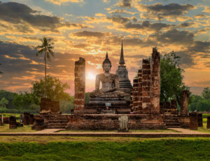 Buddha statue and pagoda Wat Mahathat temple with dramatic syk sunset, Sukhothai Historical Park, Thailand